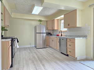 Kitchen with light wood finish cabinets, stainless steel appliances, a textured ceiling, light wood-style flooring, and backsplash