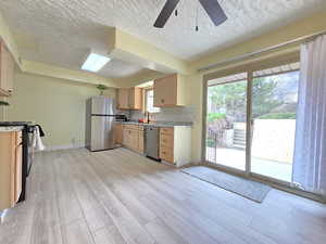 Kitchen with light wood finish cabinets, stainless steel appliances, light wood-style flooring, decorative backsplash, and a ceiling fan