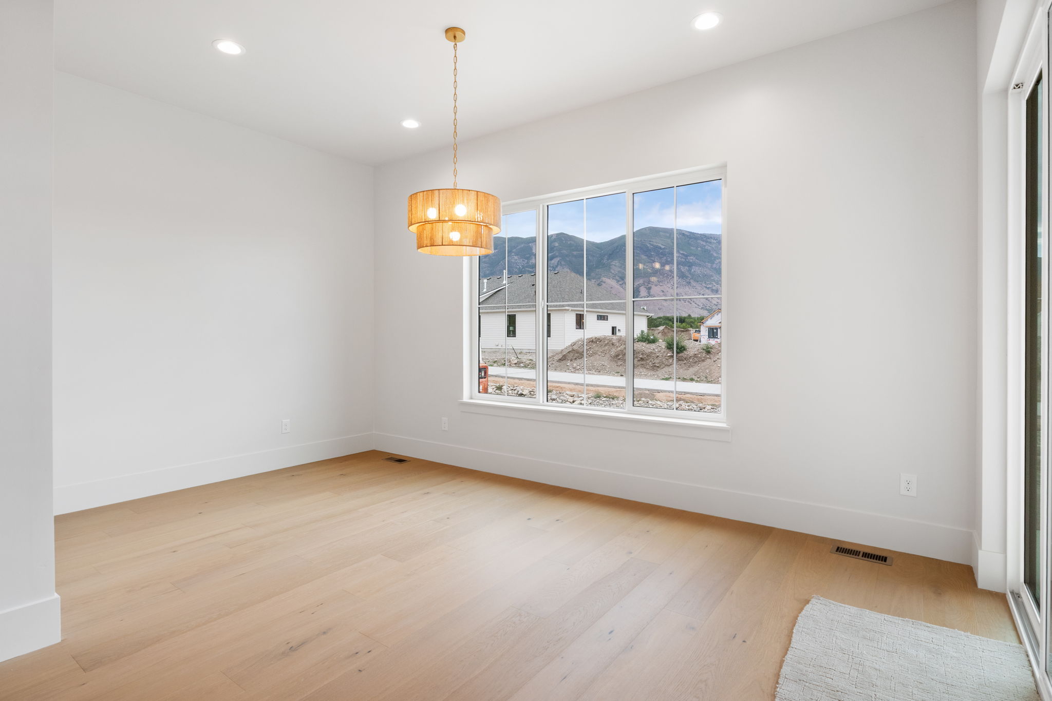 Spacious room featuring light wood-finish flooring, a large multi-pane window, recessed lighting, a modern tiered chandelier, and white wall finishes
