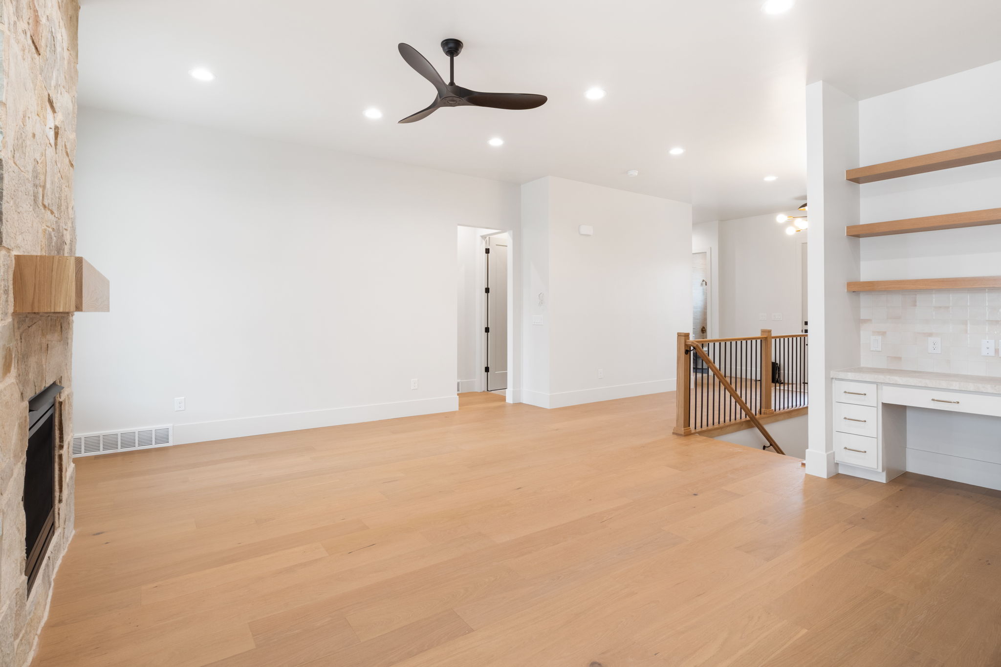 Spacious room featuring light wood-finish flooring, a stone-clad fireplace with a wood mantel, and recessed lighting