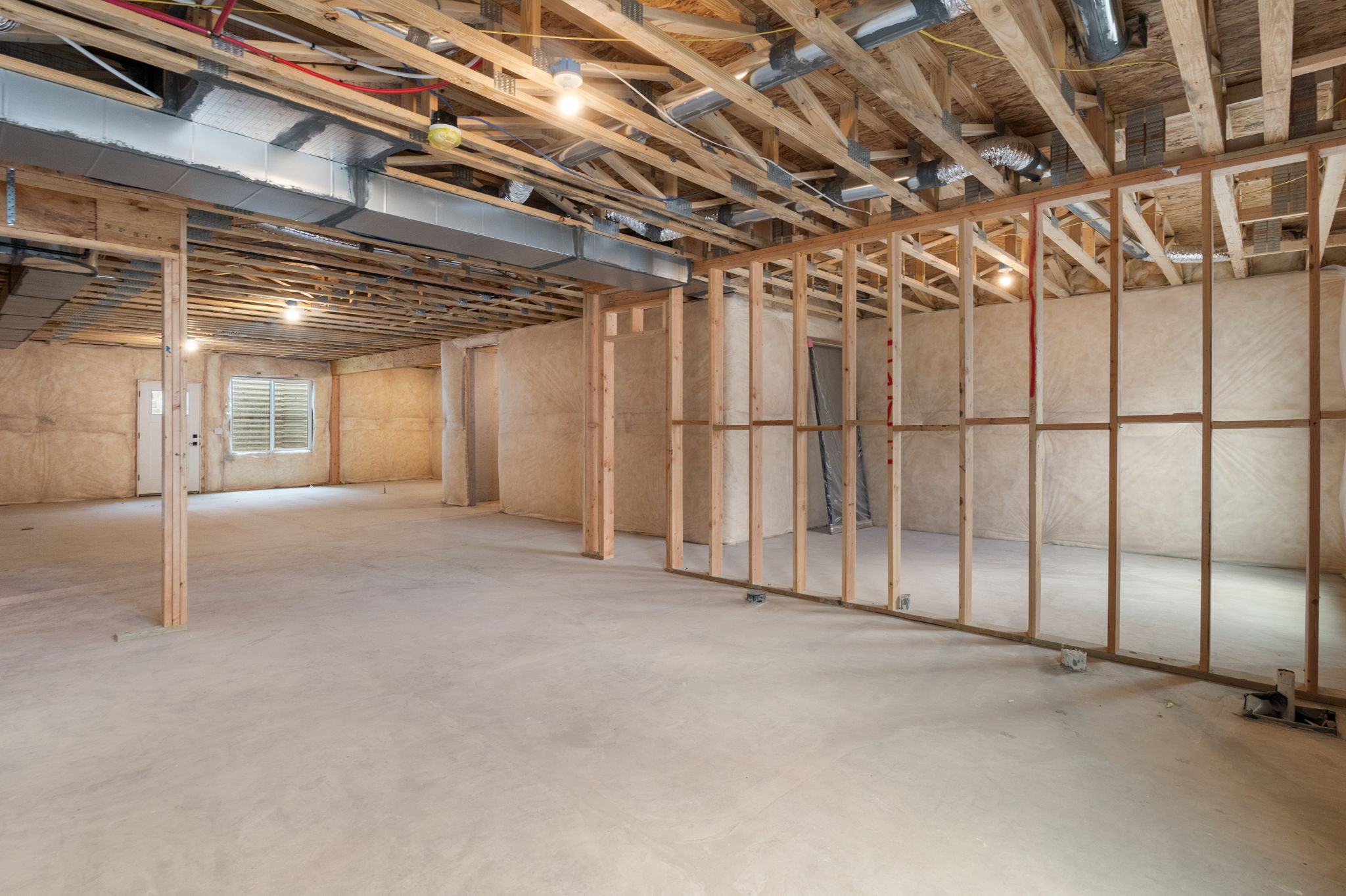 Unfinished basement featuring exposed wood joists, concrete flooring, framed wall partitions, a window with horizontal blinds, and visible HVAC ductwork