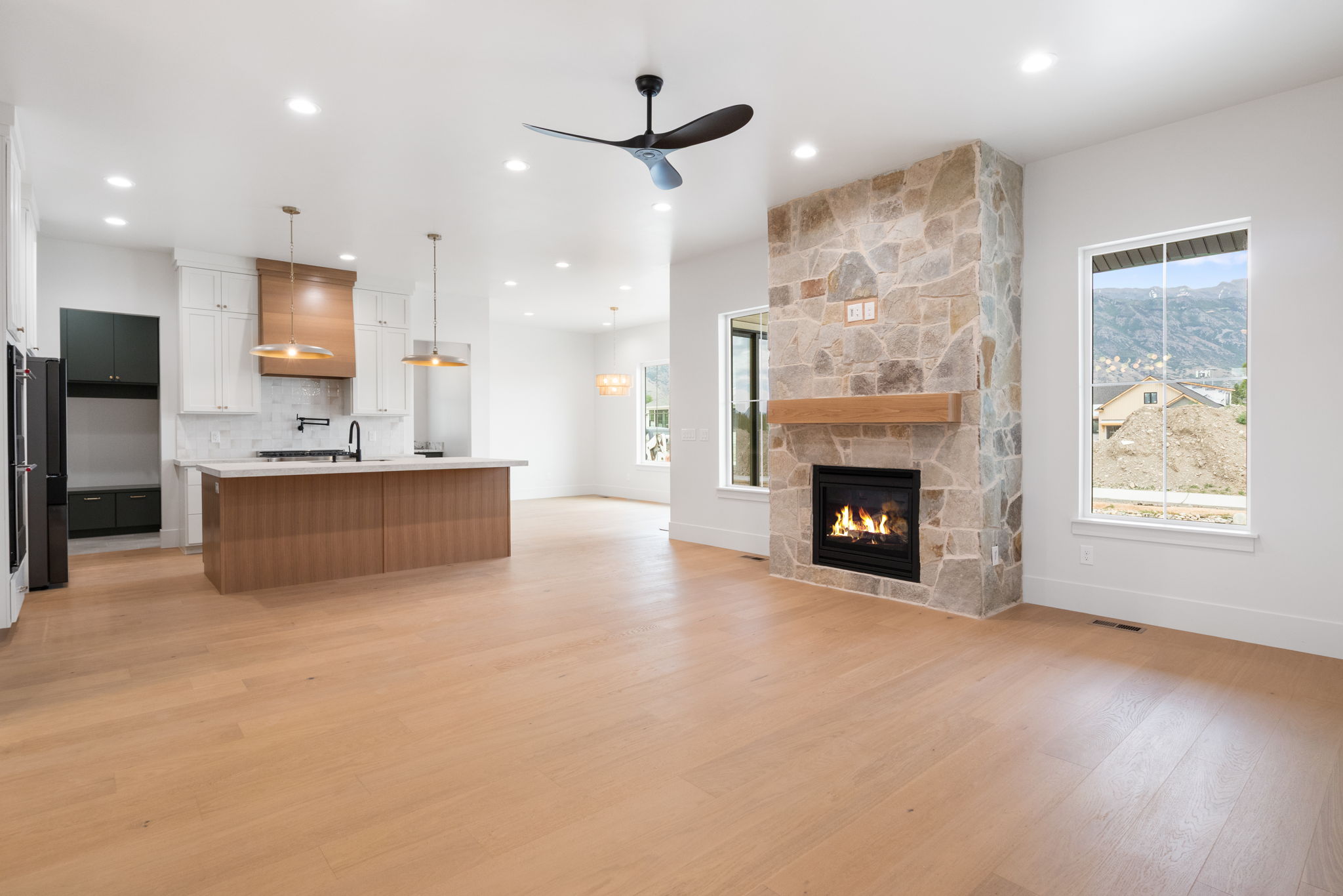 Spacious open-concept living area featuring a stone-clad fireplace with a wood mantel, light wood-finish flooring, and recessed lighting
