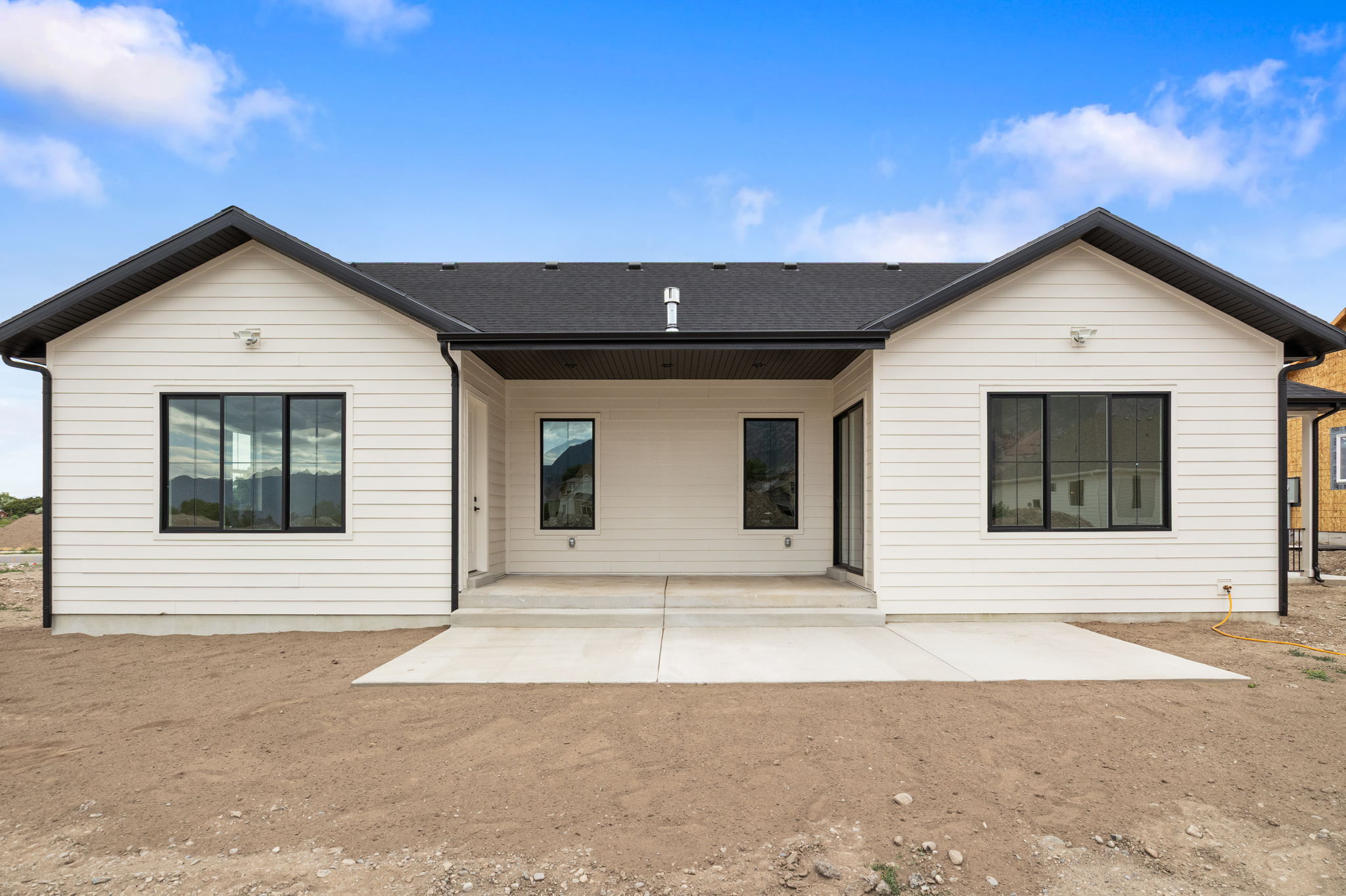 Rear exterior featuring white horizontal siding, a black shingle roof, and a concrete patio