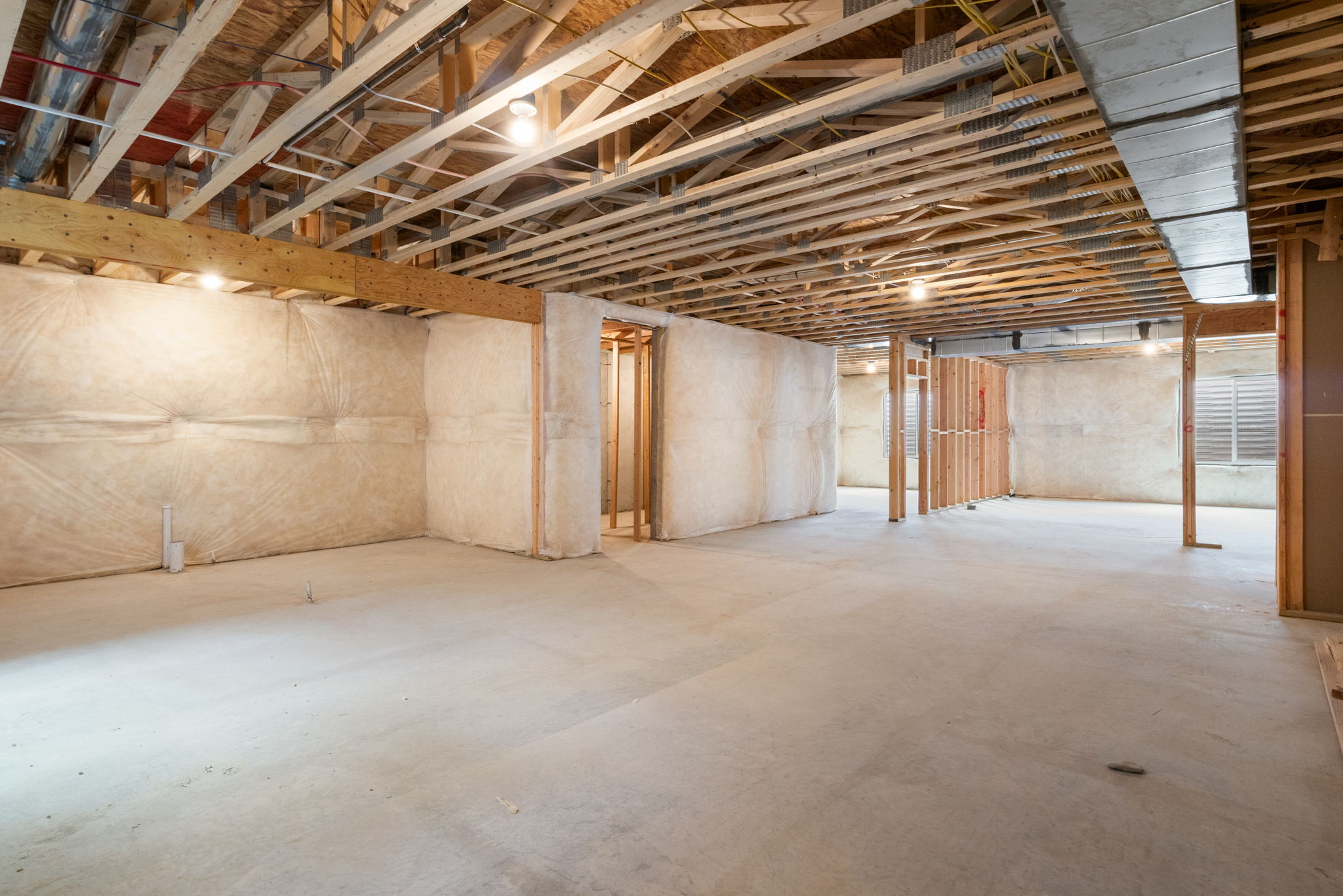 Expansive unfinished basement featuring an open floorplan, concrete flooring, exposed wood ceiling joists, ceiling-mounted lighting fixtures, and framed partition walls
