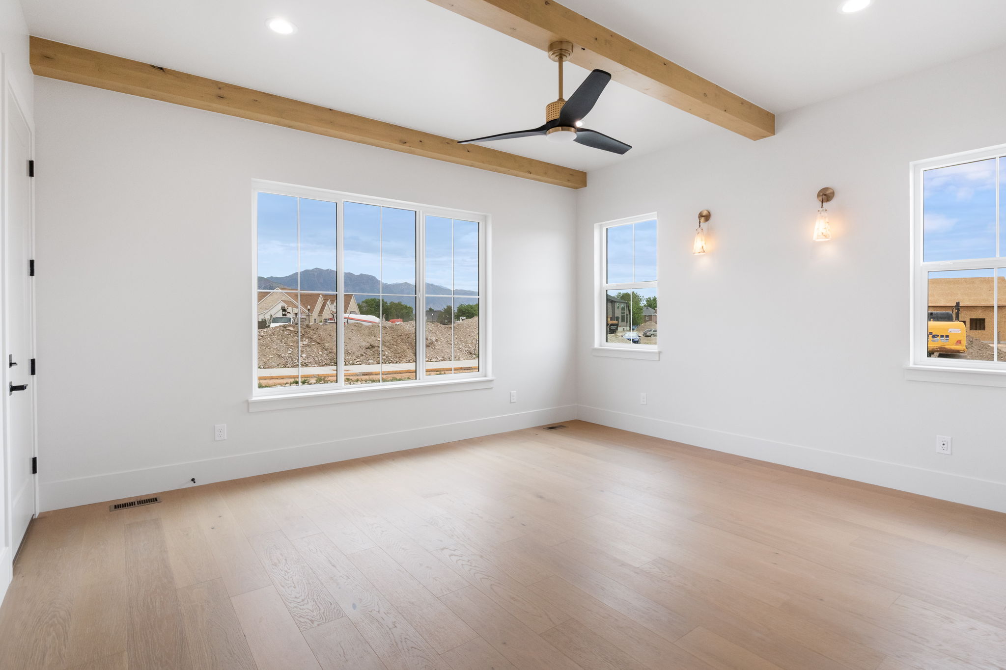 Spacious interior featuring wood-finish flooring, exposed ceiling beams, a modern ceiling fan, recessed lighting, and multiple windows with views of mountains