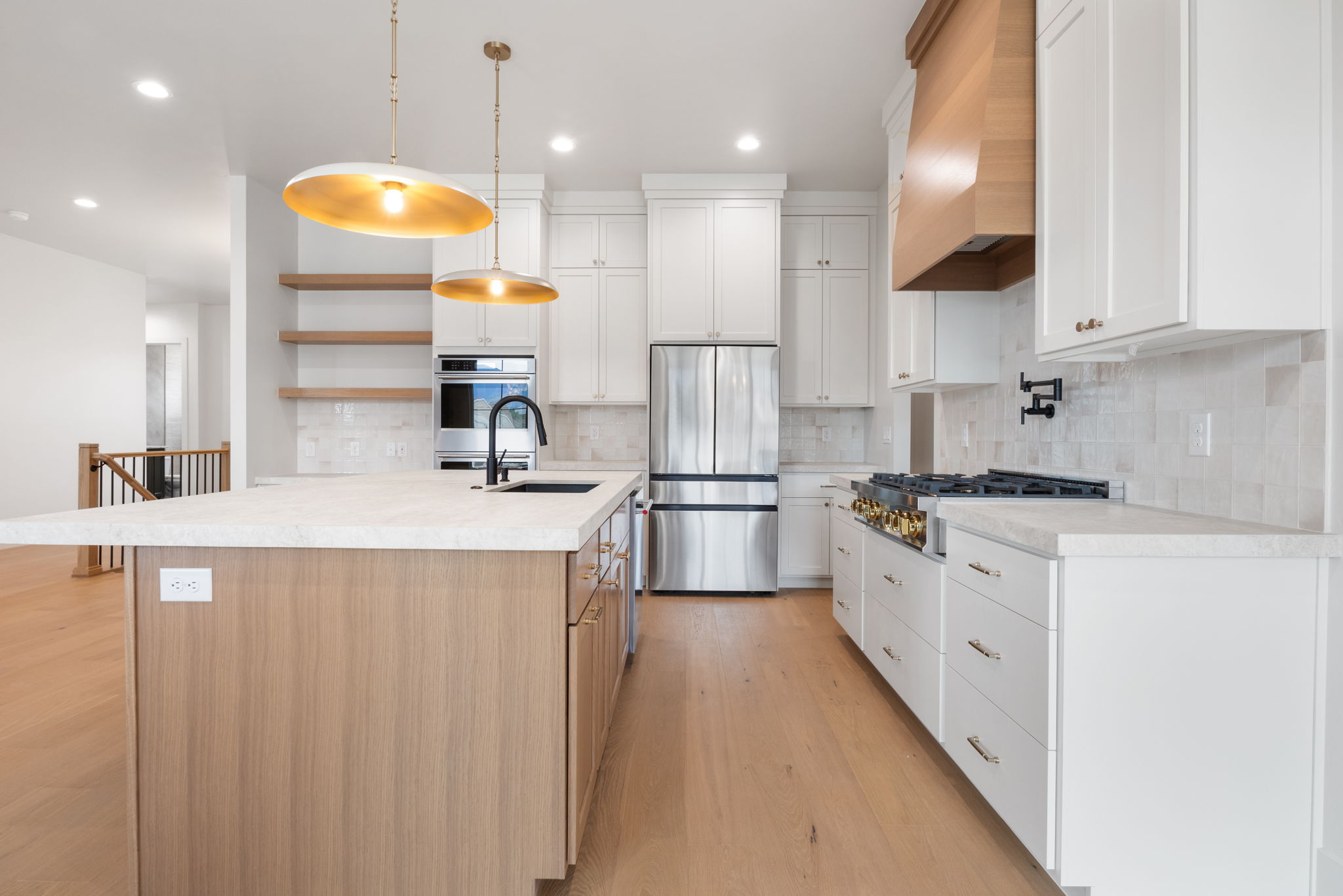 Modern kitchen featuring an expansive center island with an undermount sink, pendant lighting, professional-grade stainless steel appliances, and wood-finish flooring
