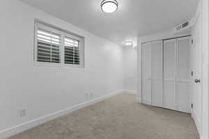 Unfurnished bedroom with light colored carpet, a closet, and a textured ceiling