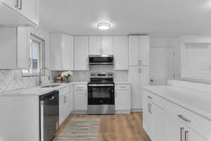 Kitchen featuring stainless steel appliances, white cabinetry, light wood-style flooring, and backsplash