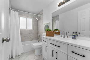 Full bath featuring vanity, light marble finish floors, and shower / bath combo