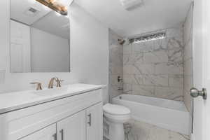 Bathroom featuring vanity, light marble finish flooring, and washtub / shower combination