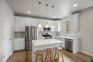 Kitchen with stainless steel appliances, white cabinets, a kitchen bar, and decorative light fixtures