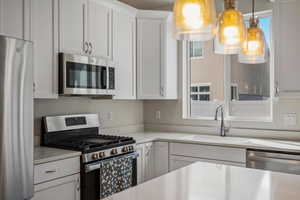 Kitchen featuring stainless steel appliances, white cabinets, and light stone counters