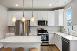 Kitchen featuring white cabinetry, stainless steel appliances, a kitchen bar, and light stone counters