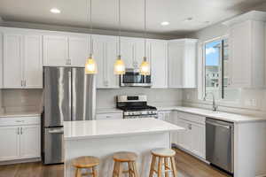 Kitchen with stainless steel appliances, white cabinets, a kitchen bar, hanging light fixtures, and dark wood-style floors