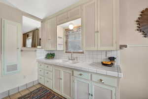 Kitchen featuring tile countertops, backsplash, light tile patterned flooring, and cream cabinets