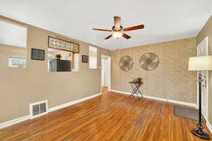 Unfurnished living room featuring wallpapered walls, hardwood / wood-style floors, a ceiling fan, and an accent wall