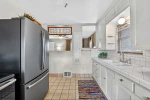 Kitchen with tile countertops, a ceiling fan, white cabinets, and light tile patterned floors