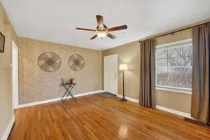 Spare room featuring an accent wall, light wood finished floors, ceiling fan, and wallpapered walls