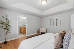 Bedroom featuring a raised ceiling, light wood-type flooring, and ensuite bathroom