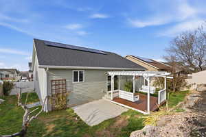 Rear view of property with roof with shingles, a fenced backyard, roof mounted solar panels, a pergola, and a wooden deck