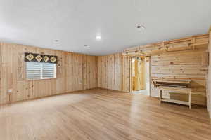 Spare room featuring wooden walls, light wood-style flooring, and a textured ceiling