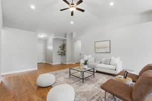 Living room featuring light wood finished floors, ceiling fan, vaulted ceiling, and arched walkways