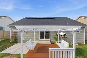 Back of property with solar panels, roof with shingles, a wooden deck, a pergola, and a patio