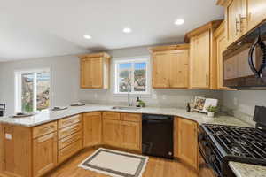 Kitchen with black appliances, light wood finish cabinets, a peninsula, light stone counters, and recessed lighting