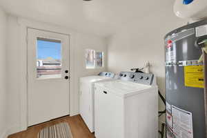Laundry area with secured water heater, wood finished floors, washing machine and dryer, and a textured ceiling