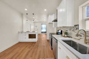Kitchen featuring white cabinetry, stainless steel appliances, decorative backsplash, light wood-style floors, and a peninsula