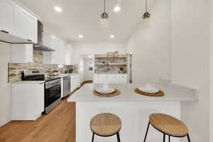 Kitchen featuring white cabinets, stainless steel appliances, a breakfast bar area, a peninsula, and light wood-style floors