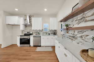 Kitchen featuring white cabinetry, stainless steel appliances, light wood-style flooring, light stone countertops, and recessed lighting