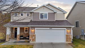 View of front of house with a porch, stone siding, an attached garage, driveway, and roof with shingles