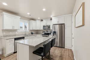 Kitchen featuring stainless steel appliances, a breakfast bar area, light wood-type flooring, light stone counters, and recessed lighting
