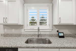 Kitchen featuring light stone counters, white cabinets, and dishwasher