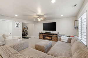Carpeted living room featuring ceiling fan, recessed lighting, and a glass covered fireplace