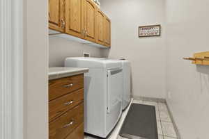 Laundry area featuring washing machine and dryer, light tile floors, and cabinet space