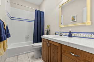Hall bathroom featuring vanity, shower/bath combo with decorative tile, and light tile floors