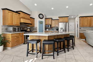 Kitchen featuring a kitchen bar, wood finish cabinets, pantry, a spacious island, light countertops, and decorative backsplash