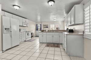 Downstaris kitchen featuring a peninsula, white appliances, light tile floors, and white cabinetry