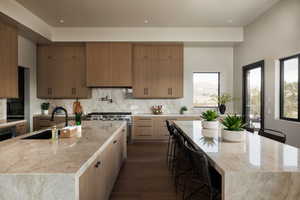 Kitchen featuring light stone countertops, a large island, a breakfast bar, decorative backsplash, and dark wood-style floors