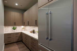Kitchen featuring built in refrigerator, dark wood-type flooring, backsplash, modern cabinets, and light stone counters