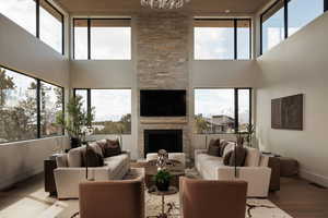 Living area with a stone fireplace, wood finished floors, a high ceiling, and suspended lighting