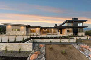 Back of property at dusk with stone siding and a patio area