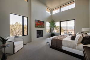 Bedroom with carpet floors, a glass covered fireplace, access to outside, a high ceiling, and multiple windows