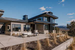 Rear view of house featuring stone siding, a patio area, a chimney, and a mountain view