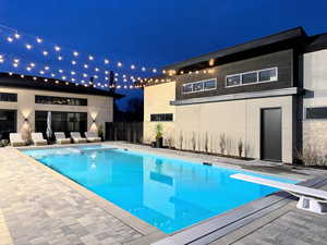 Pool at twilight featuring a patio, a pool with connected hot tub, and a diving board
