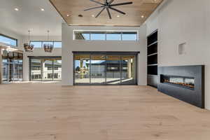Unfurnished living room with built in features, a glass covered fireplace, hanging lights, light wood finished floors, and a high ceiling