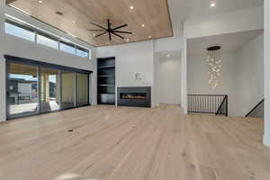 Unfurnished living room with built in shelves, light wood finished floors, recessed lighting, a large fireplace, and a high wooden ceiling