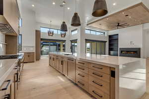 Kitchen featuring a large island, light wood finished floors, light stone countertops, a glass covered fireplace, and a high ceiling
